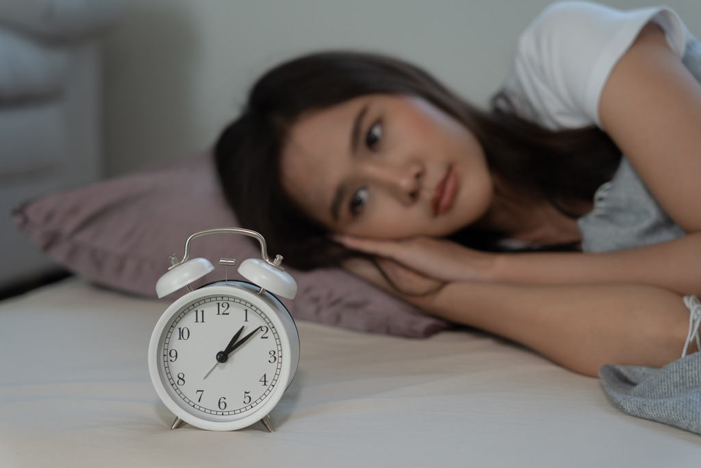 A Woman Laying On Her Side In Bed Looking At A Clock Can An OBGYN Help You With Hormones