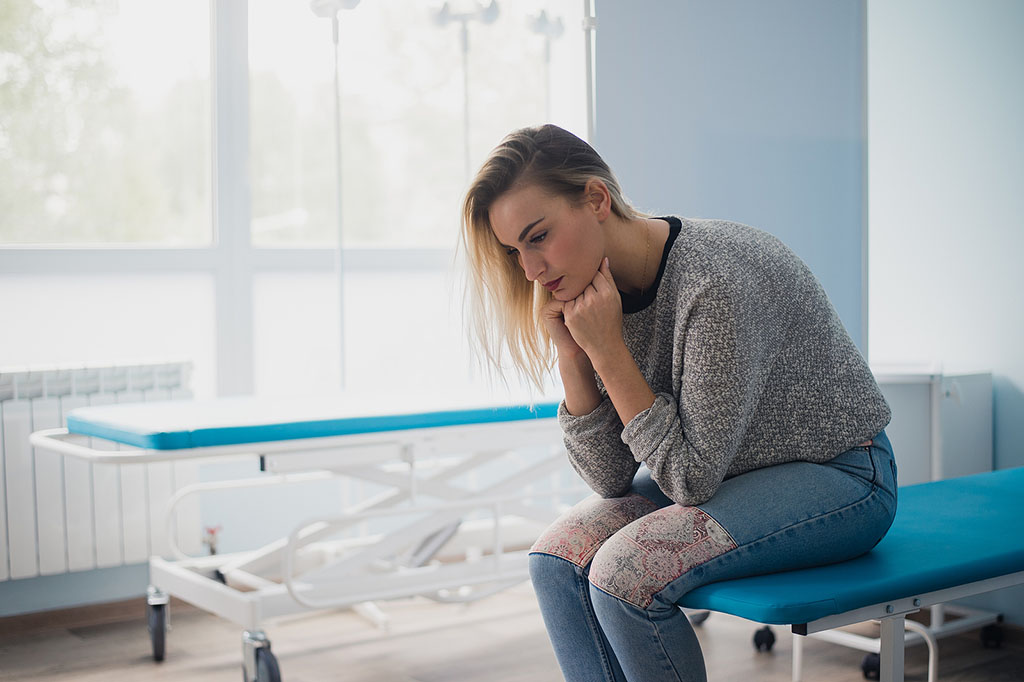 A Woman Sitting On An Exam Table Waiting For The Obgyn Doctor What Causes Uterine Cancer
